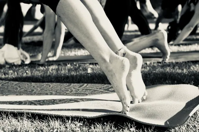 Bare feet rise onto the toes on a patterned mat during an outdoor yoga class, photographed in black and white.