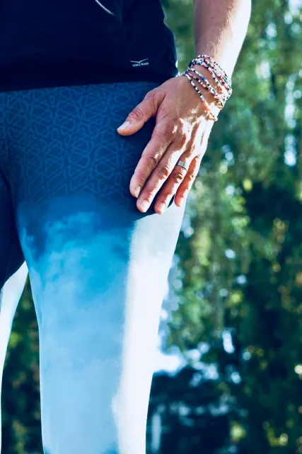 A close view of a hand resting against blue patterned leggings, with bracelets catching the outdoor sunlight.
