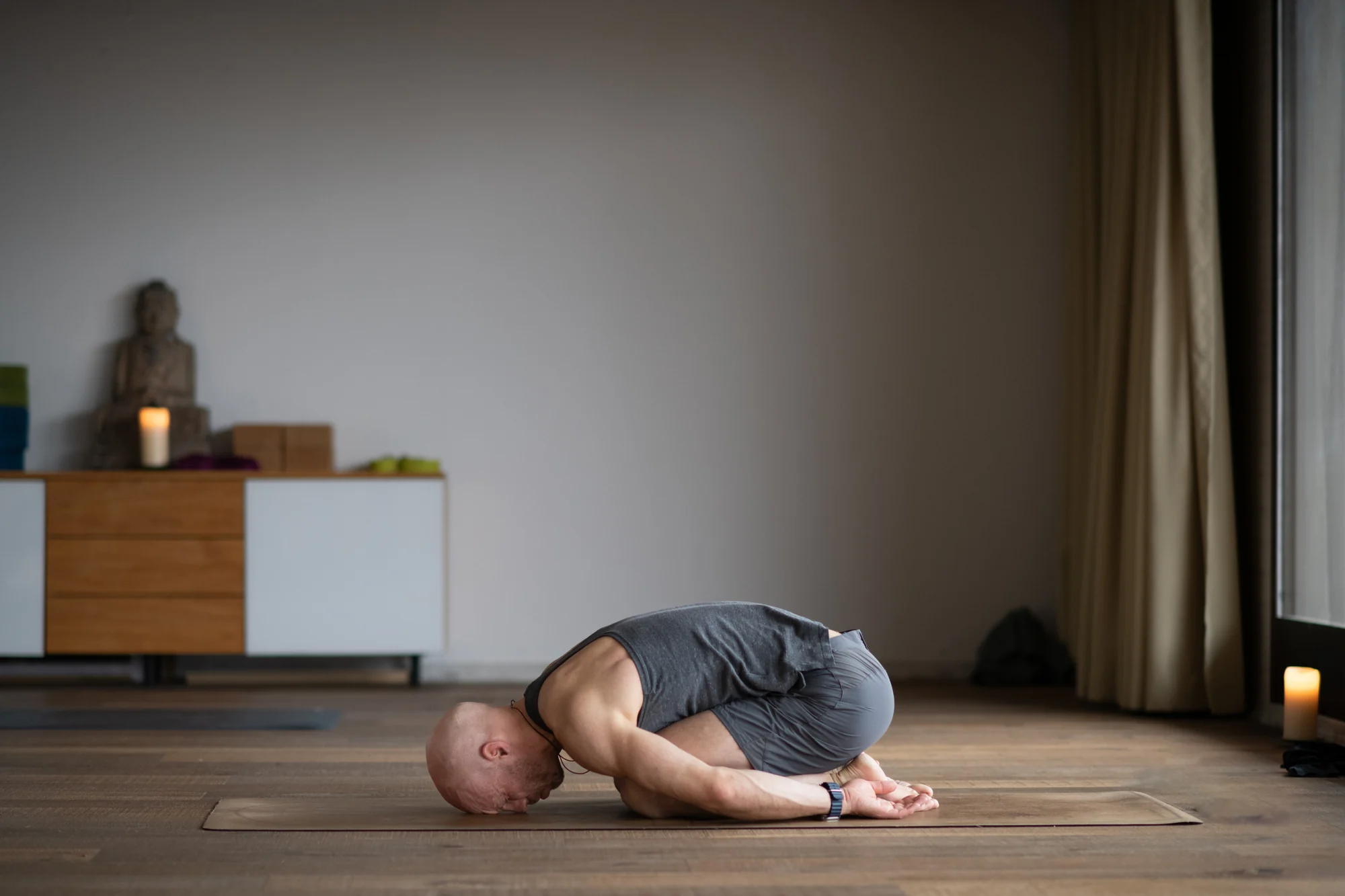 Felix rests in Child’s Pose with the torso folded toward the thighs, forehead lowered and arms beside his legs.