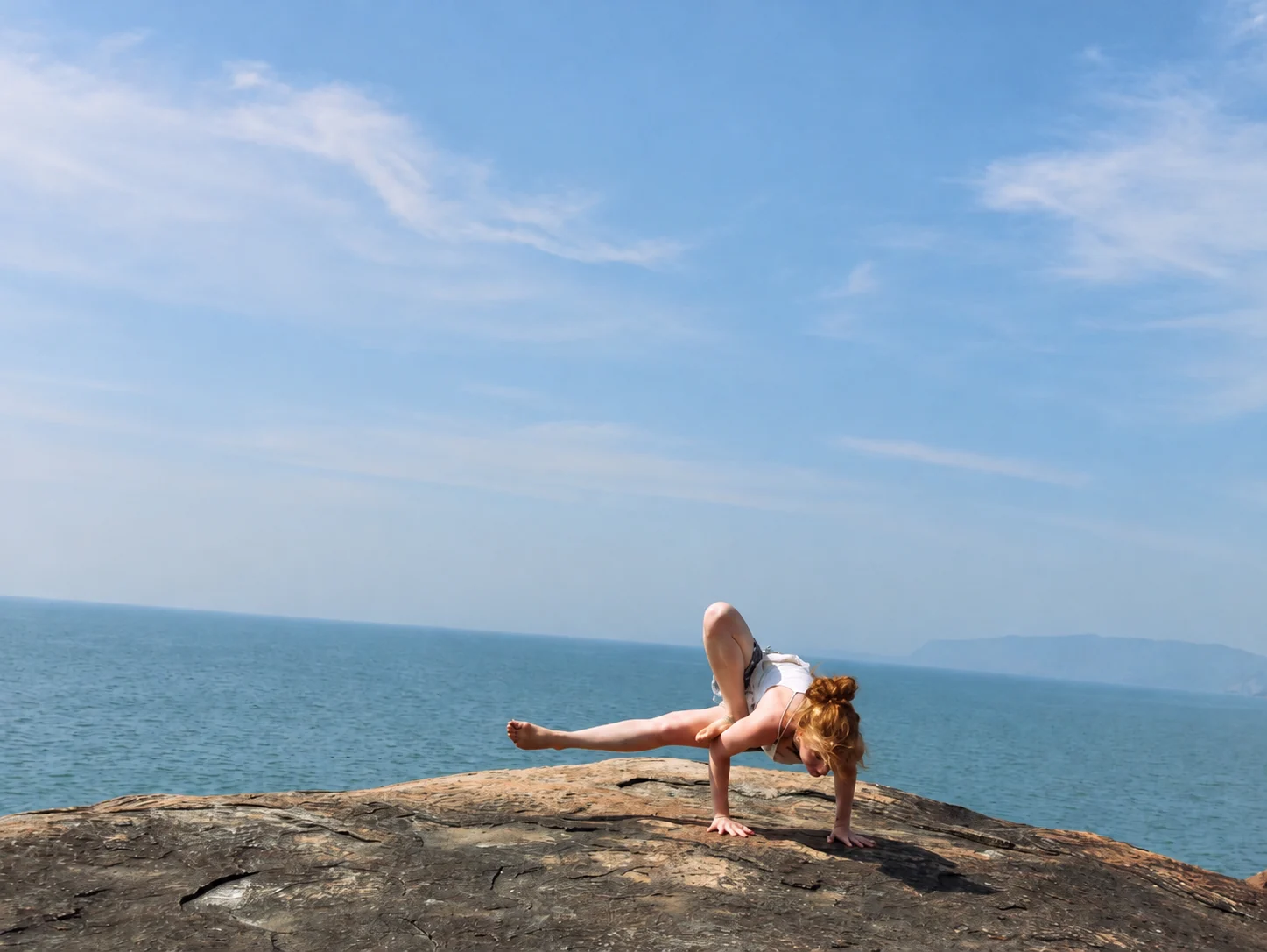 Une pratiquante tient la posture de la libellule, un pied en appui près du haut d’un bras et l’autre jambe tendue sur le côté.