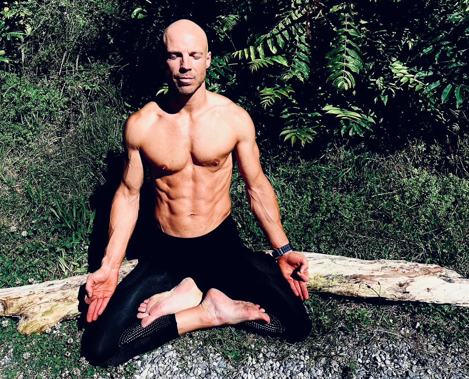 Felix sits outdoors in Lotus Pose, with each foot on the opposite thigh and his hands resting on his knees.