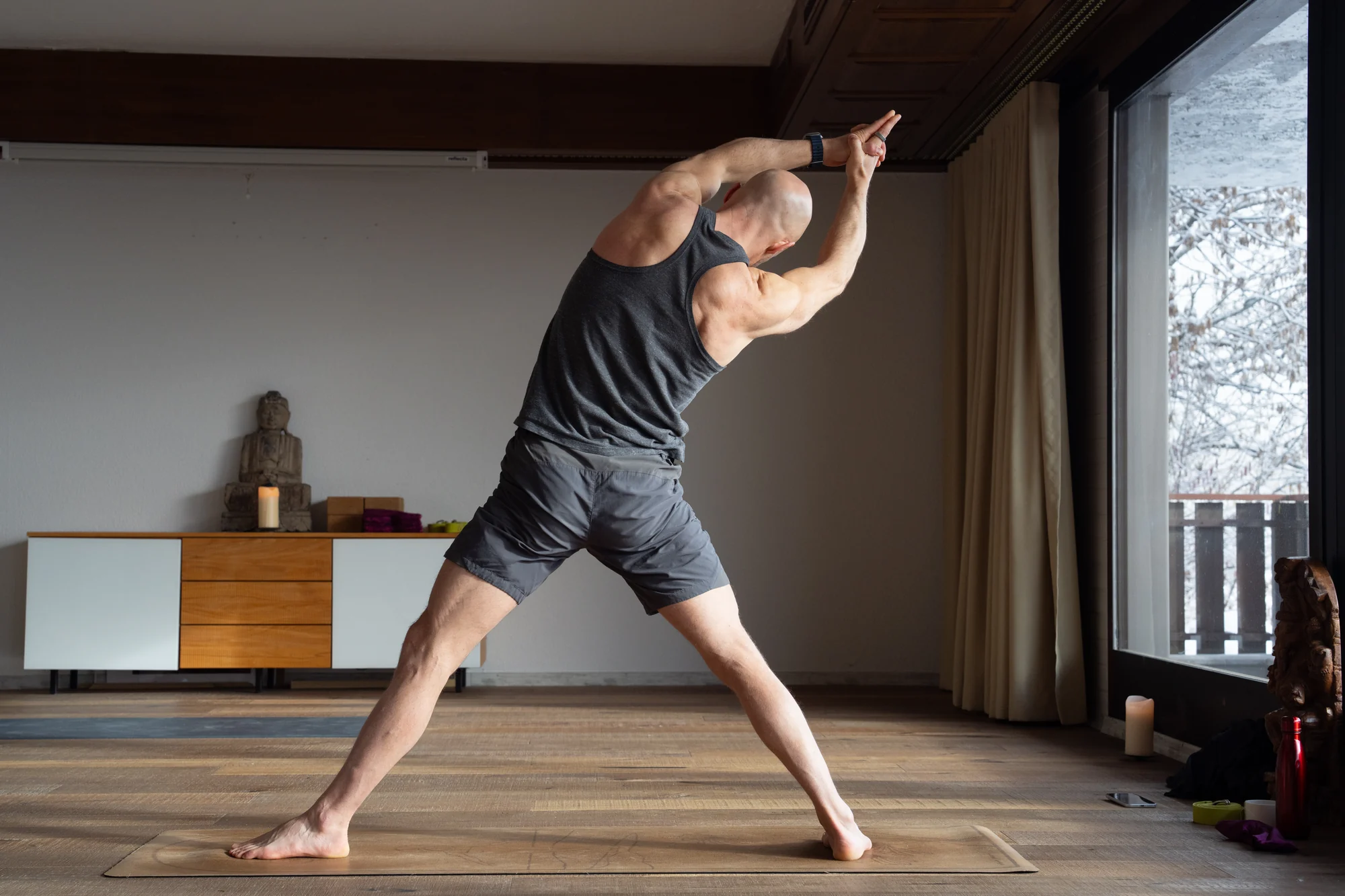 Felix se tient debout jambes tendues et écartées, en inclinaison latérale avec les mains jointes au-dessus de la tête, dans une variation du triangle inversé.