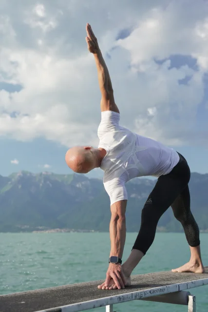 Felix tient le triangle étiré au bord du lac, vu de dos, une main près du pied avant et le bras opposé levé.