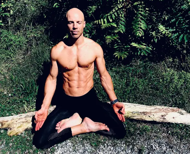 Felix est assis dehors dans la posture du lotus, chaque pied sur la cuisse opposée et les mains posées sur les genoux.