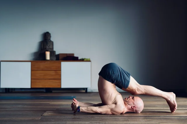 Felix tient la posture de la charrue, les pieds au sol derrière la tête et les mains entrelacées derrière le dos.