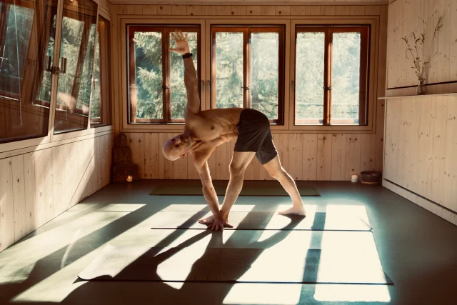 Felix tient le triangle en torsion, jambes tendues, une main près du pied avant et le bras opposé levé tandis que le buste tourne.