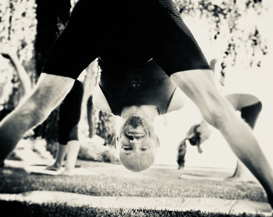 A close rear view shows a wide-legged forward bend with the head lowered between straight legs.