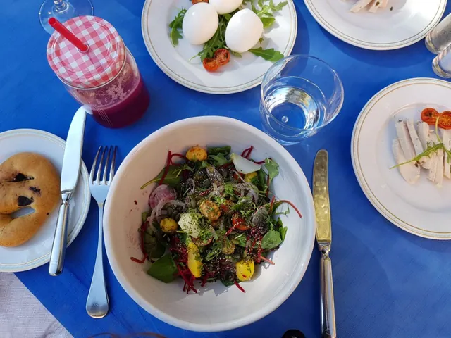 Un repas coloré avec salade, pain et boisson rose est servi sur une nappe bleue.