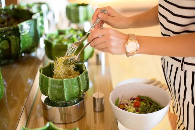 Des mains servent des pousses et des légumes dans un bol vert.