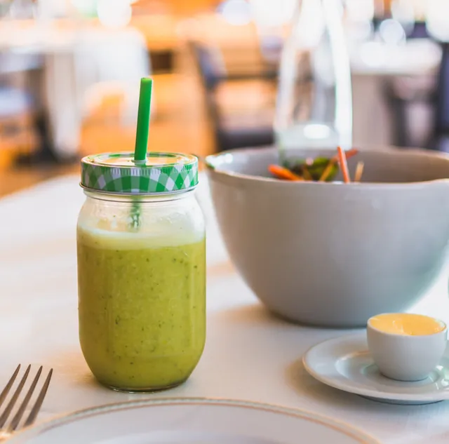 Un bocal de smoothie vert est posé sur une table à côté d’un grand bol et d’une petite tasse.