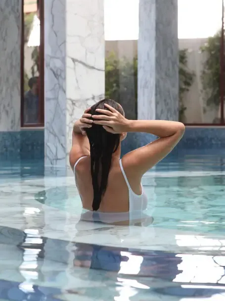 Une femme se détend dans la piscine intérieure, les mains derrière la tête, entourée de colonnes de marbre.