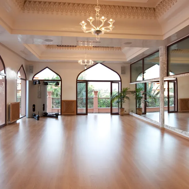 Une vaste salle de pratique avec parquet, lustres et portes cintrées ouvertes vers le jardin.