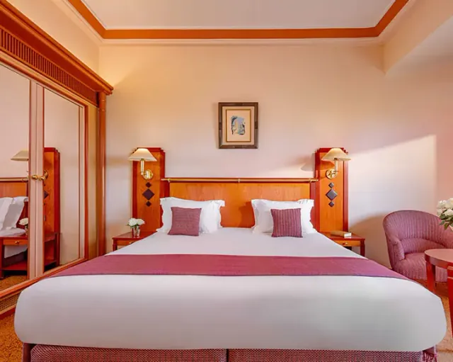 Une chambre avec un lit double, des murs roses et ocre et des textiles aux tons doux.