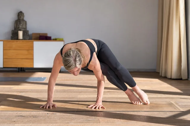 Une femme prend appui sur les deux mains, les jambes réunies sur un côté du tapis de yoga, dans une lumière vive.