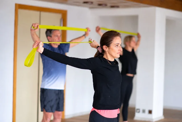 Des participants étirent leurs épaules à l’aide de sangles de yoga jaunes, avec une femme en haut noir au premier plan.