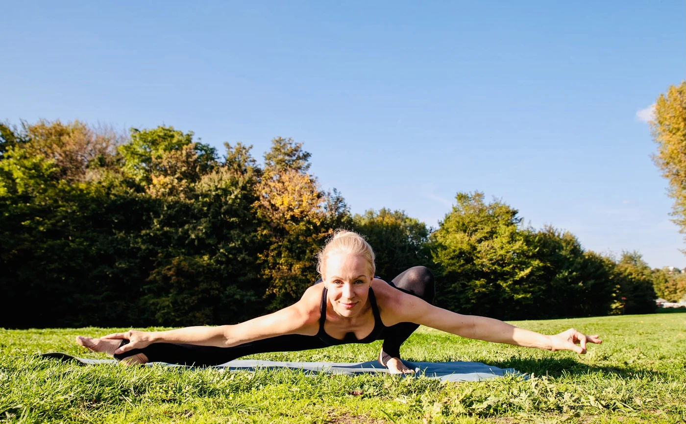 Natalya in a low yoga balance with outstretched arms, facing the camera on a sunny lawn