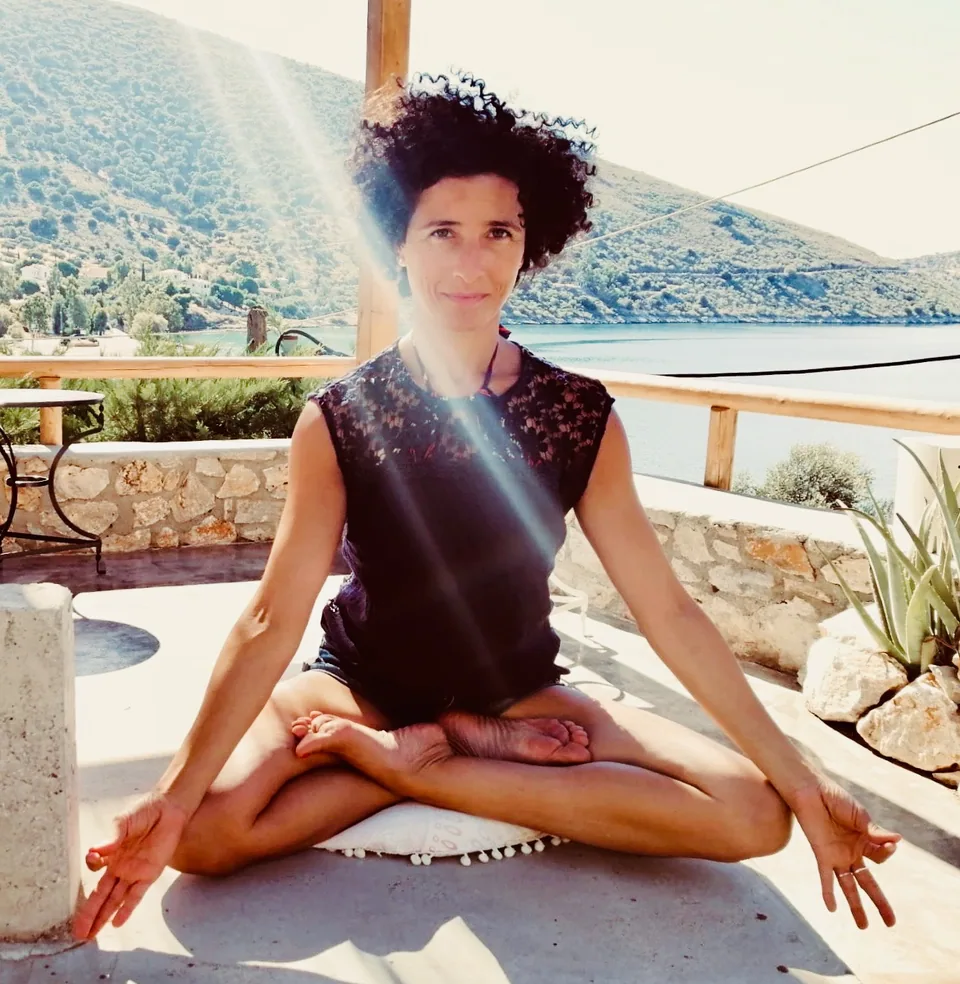 Nora seated in meditation on a sunny terrace by the sea